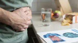 Persona con le mani sull'addome accanto a un bicchiere d'acqua e un'immagine dell'apparato digerente