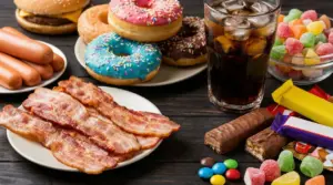 Piatto con bacon, hot dog, ciambelle, bibita gassata, caramelle e snack confezionati